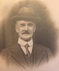Posed sepia photograph, head and shoulders of Mr. John S. Hearn. Trimed mustache, wearing a hat and white button collar shirt with narrow knotted tie, waistcoat and top coat.