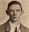 Posed sepia photograph, head and shoulders of James Nolan prior to enlisting aged 20. Freshfaced, short dark hair, wearing a white shirt with narrow knotted tie and a lighted coloured relaxed jacket.